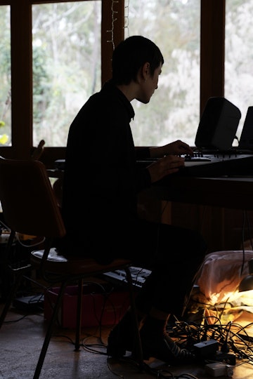 A short-haired person sits indoors at a control panel, almost silhouetted against a window