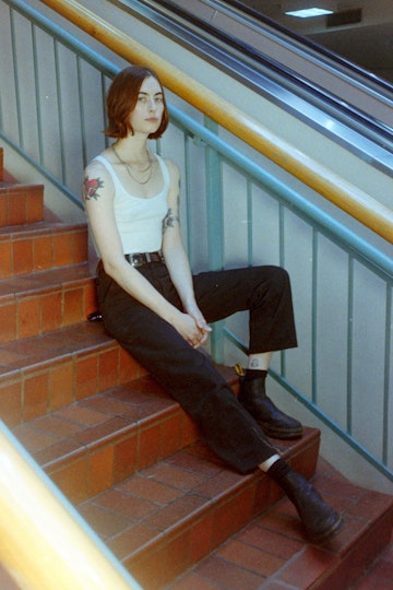 A person with chin-length hair sits on some stairs