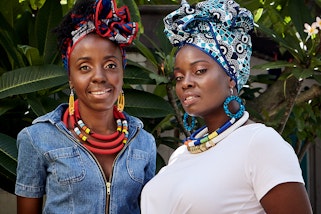 Two people wearing colourful headwraps, large earrings and necklaces