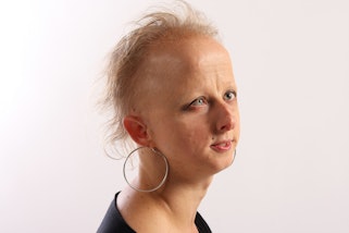 The head and shoulders of a person in partial profile with short light hair and wearing large hoop earrings