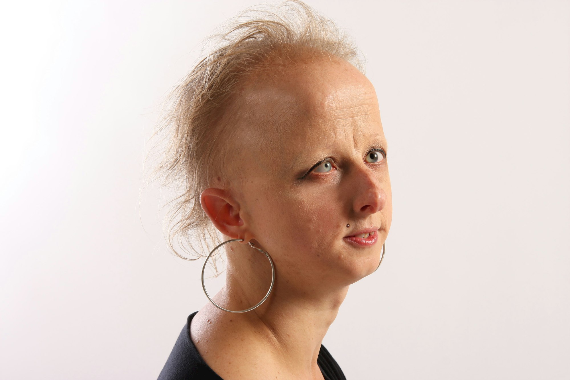 The head and shoulders of a person in partial profile with short light hair and wearing large hoop earrings