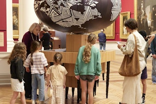 A group of adults and children in a gallery space next to a sculptural installation