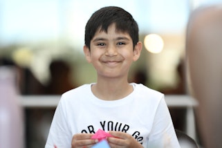 A smiling child holding a piece of pink paper in their hands
