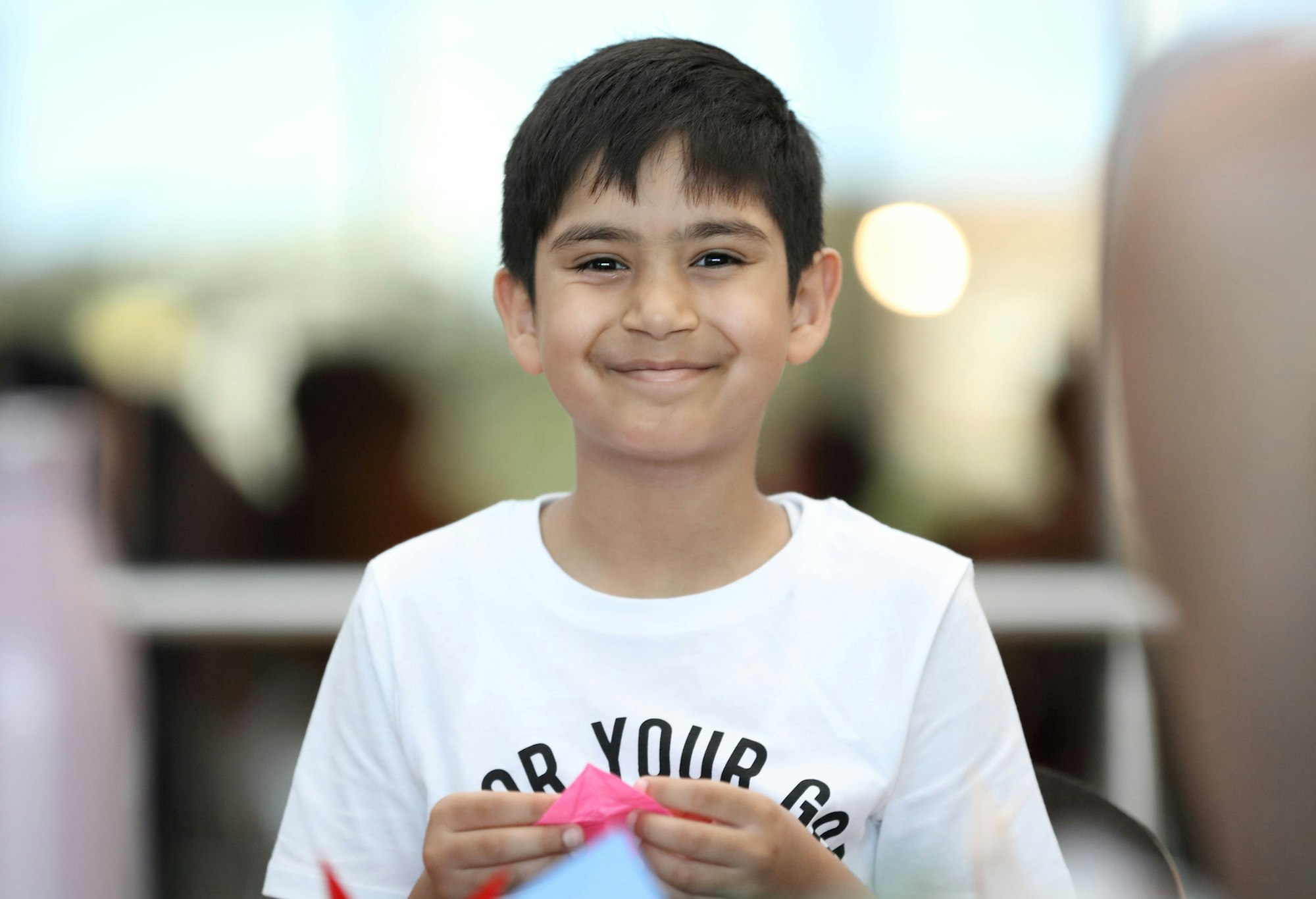 A smiling child holding a piece of pink paper in their hands