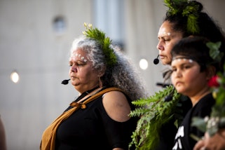 Three people with dots of white paint on their foreheads, wearing  black clothes and body ornaments made from plants