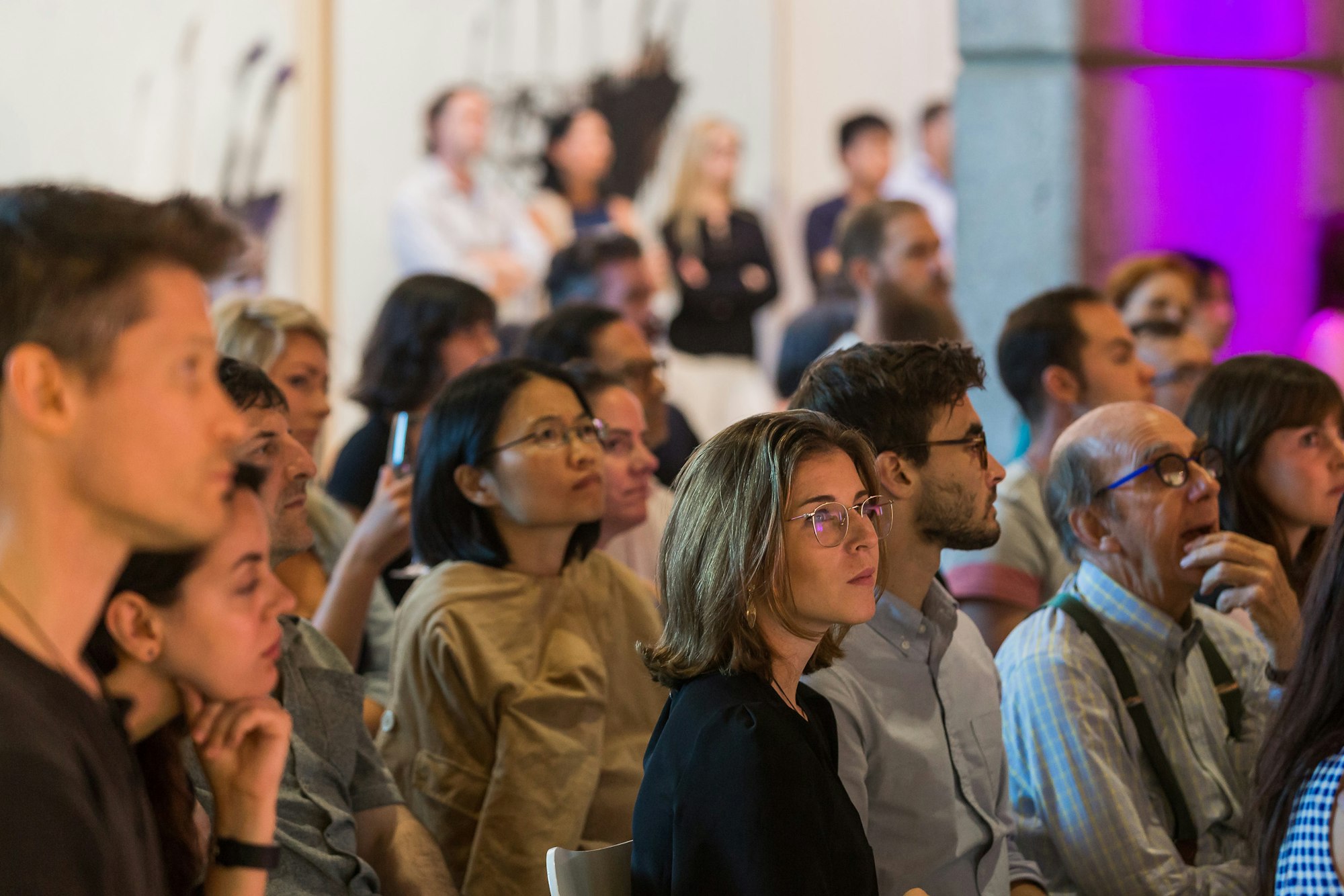 Around 20 people of different backgrounds, ages and genders, most seated