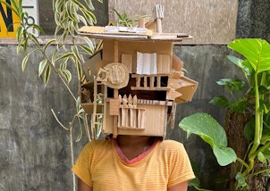 A person with a house-like object made from cardboard on their head like a mask