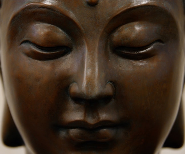 The face of a bronze sculpture, with arched eyebrows, downcast eyes, a straight nose and closed mouth