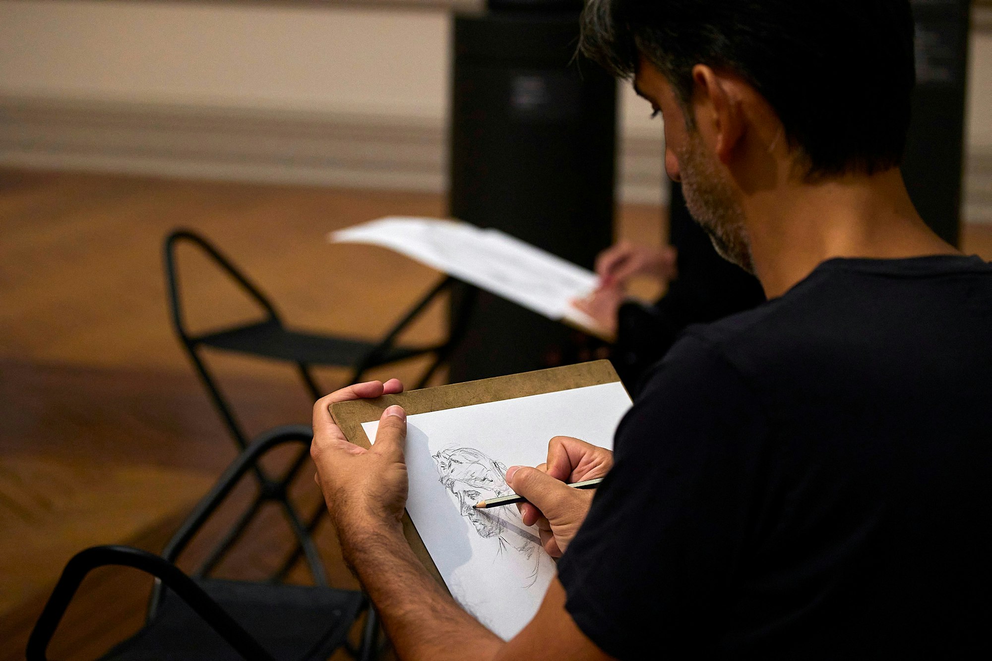 A person draws a head with a pencil on a piece of paper, leaning on a clipboard