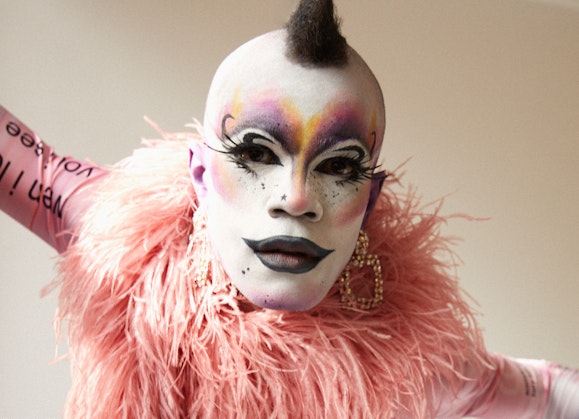 A person in heavy make-up wearing pale pink features and big earrings