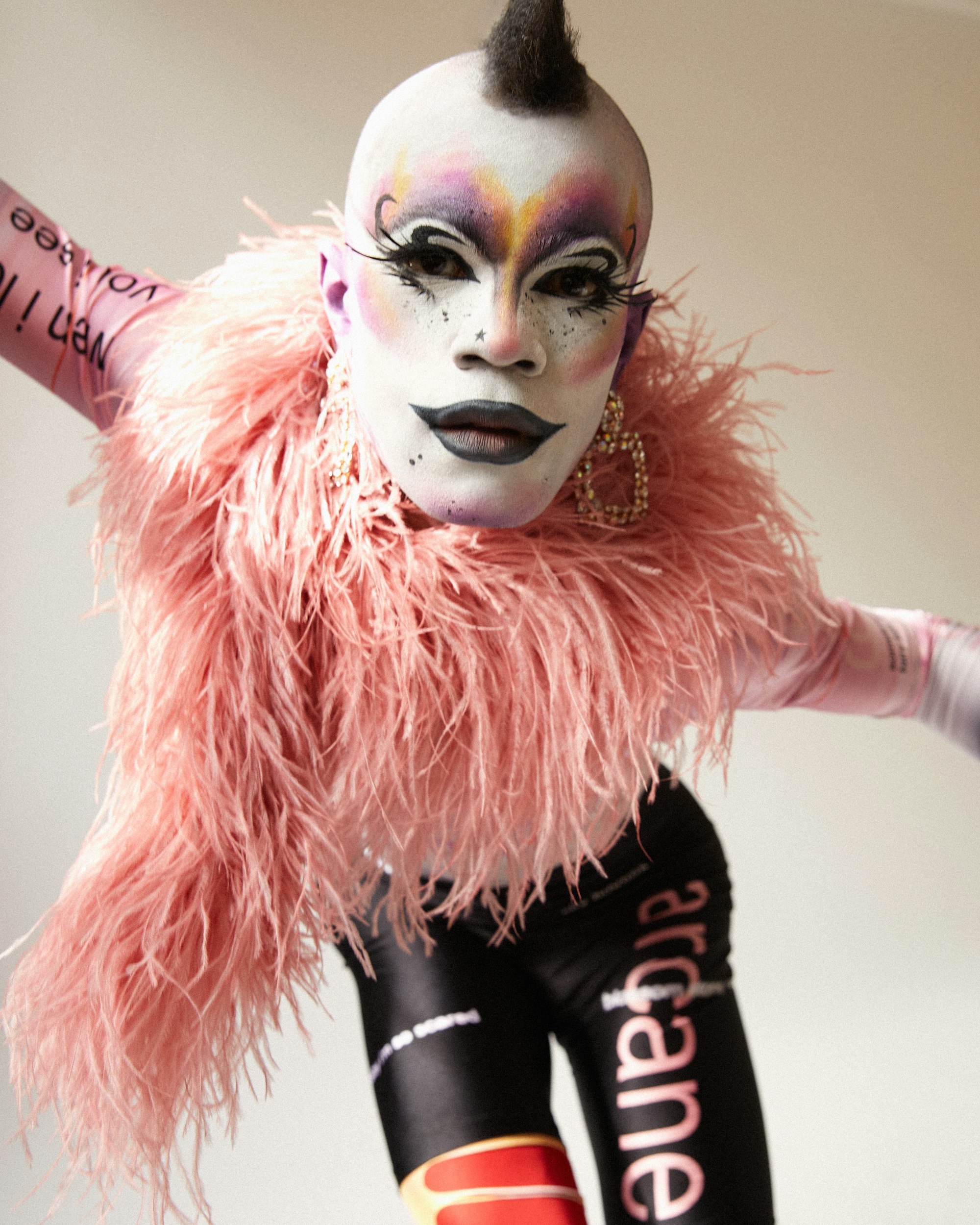 A person in heavy make-up wearing pale pink feathers and big earrings