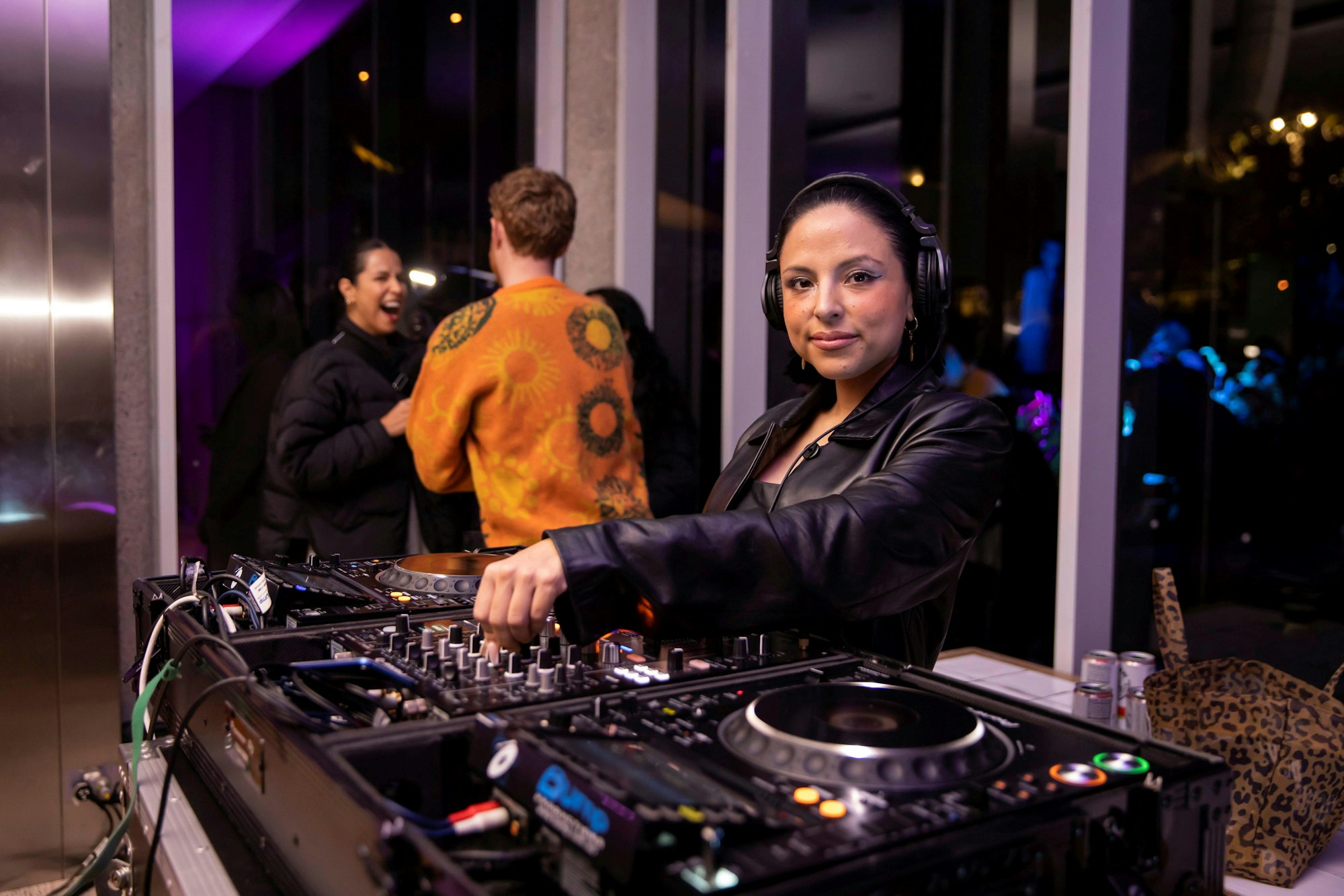 A person wearing headphones stands in front of two turntables and a mixing desk