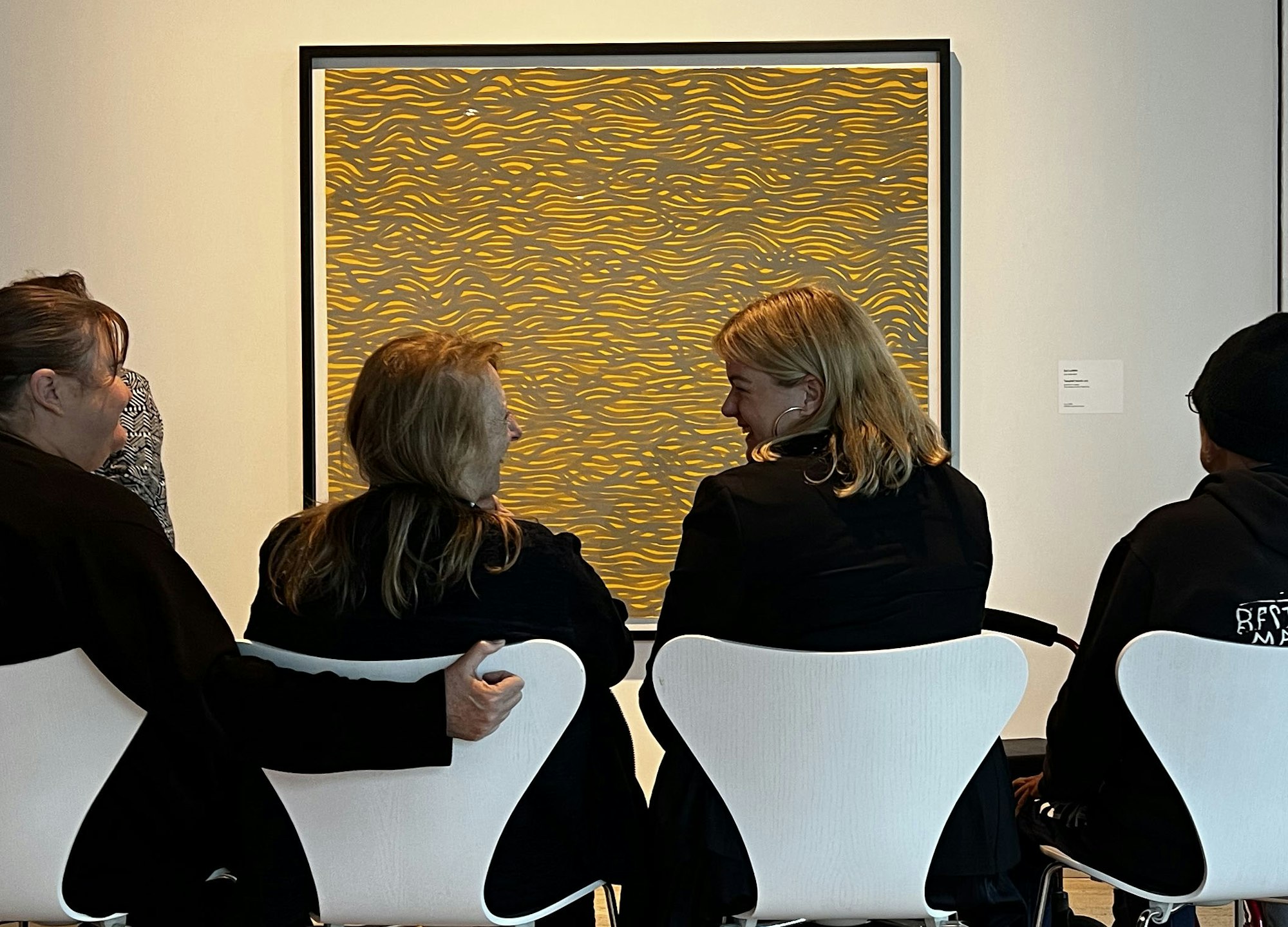 People sit on chairs in front of a framed artwork on a wall