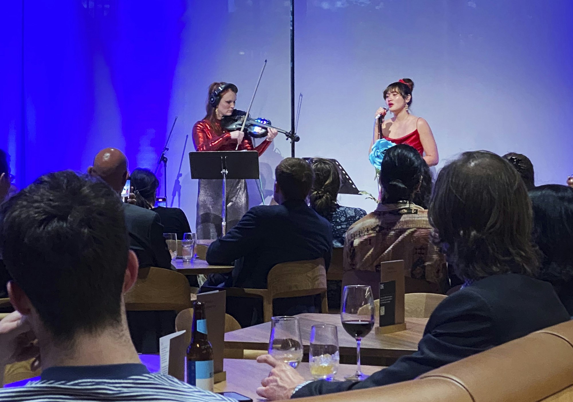 A singer and a violinist perform in front of an audience seated at tables