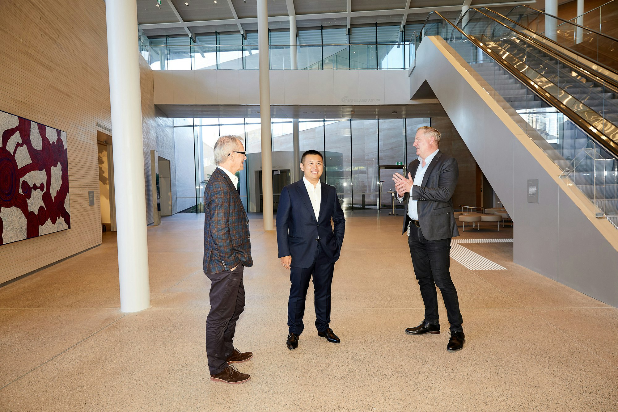 Art Gallery of New South Wales director Michael Brand, Aqualand managing director Jin Lin, and Art Gallery director of development John Richardson, in the Aqualand Atrium of the Art Gallery’s new building. Artwork in background: Betty Kuntiwa Pumani ‘Antara’ 2017, Art Gallery of New South Wales, acquired with funds provided by the AGNSW Board of Trustees 2017 © Betty Kuntiwa Pumani. Photo © AGNSW, Jenni Carter