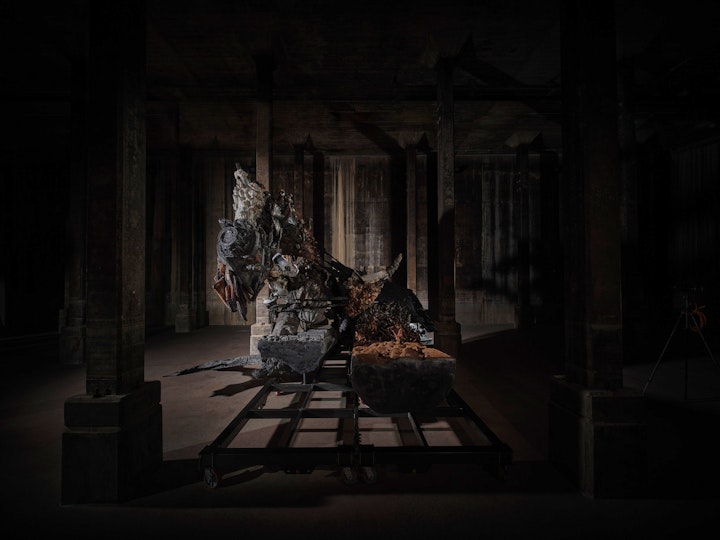 A large sculptural form in a very dark room with columns