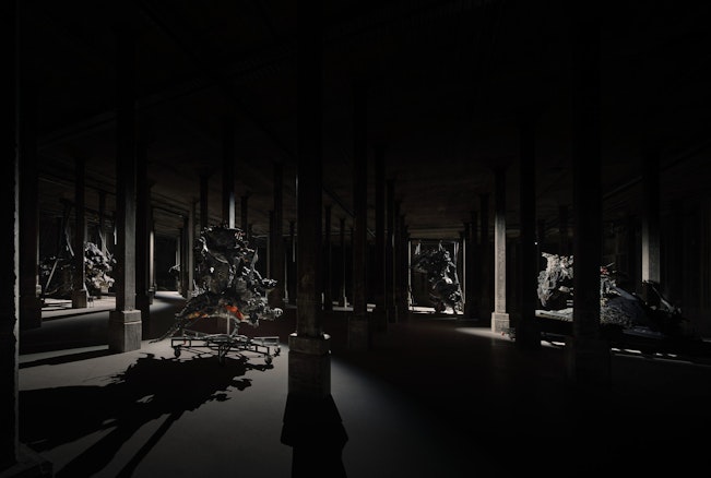 Several large sculptural forms in a very dark room with columns