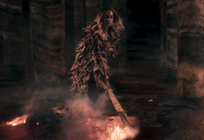 A cloaked person holds a firestick to the ground