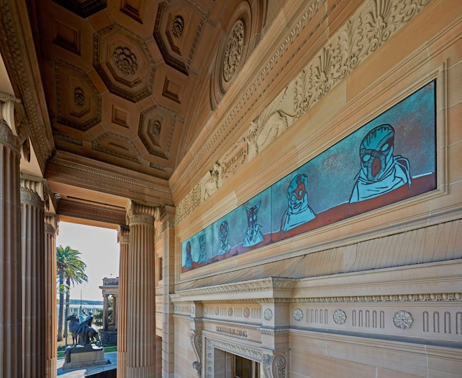 Part of an ornate sandstone building with a panel featuring hooded heads