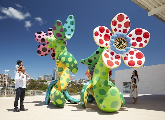 Four people look at a colourful sculpture of flowers with spots on an outdoor terrace
