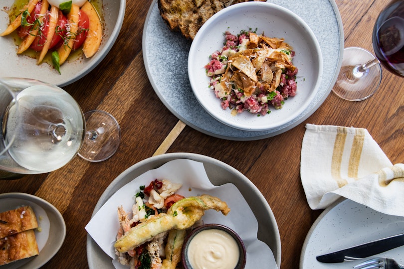 Plates of food, a wine glass, crockery, cutlery and a napkin