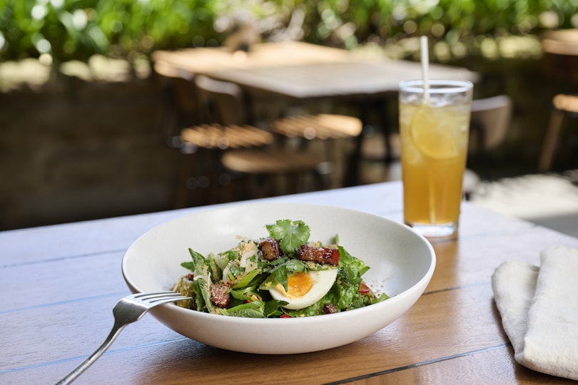 A bowl of salad, fork, napkin and glass on an outdoor table