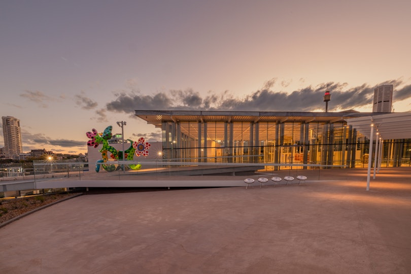 An outdoor terrace, partly roofed, in the evening with a flower sculpture at the far end