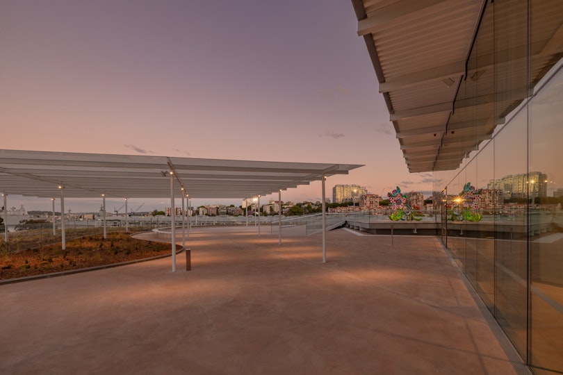 An outdoor terrace, partly roofed, in the evening with a flower sculpture at the far end