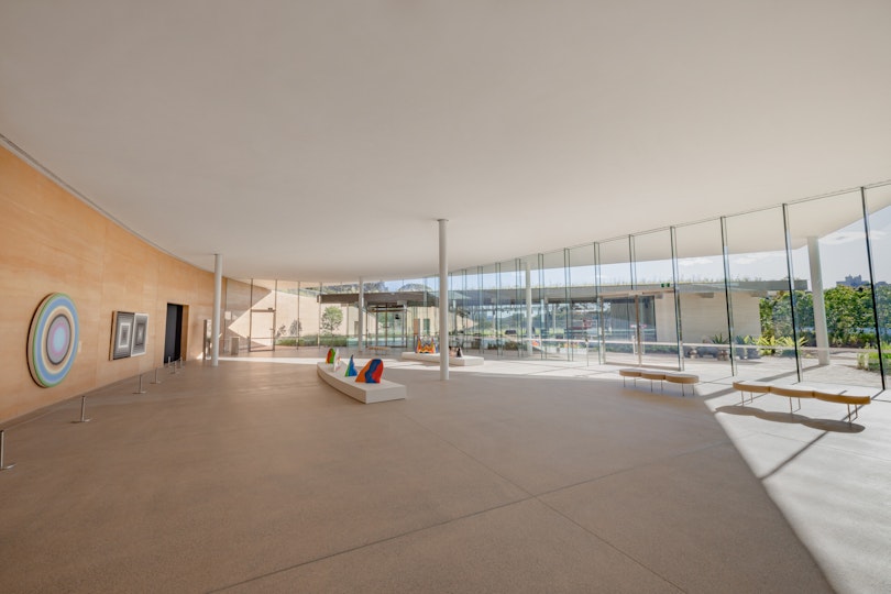 A large gallery space with sculptures on plinths and a glass wall on right looking outdoors