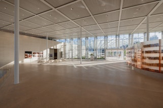 A large room with a few thin white columns and a glass wall at the far end