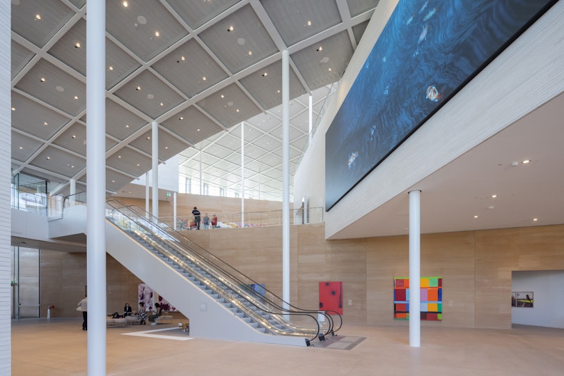 Inside a large gallery space with curved roof and escalator between levels