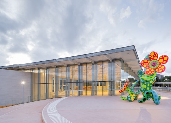 A large sculpture of spotted flowers on a terrace outside of a glass-walled building