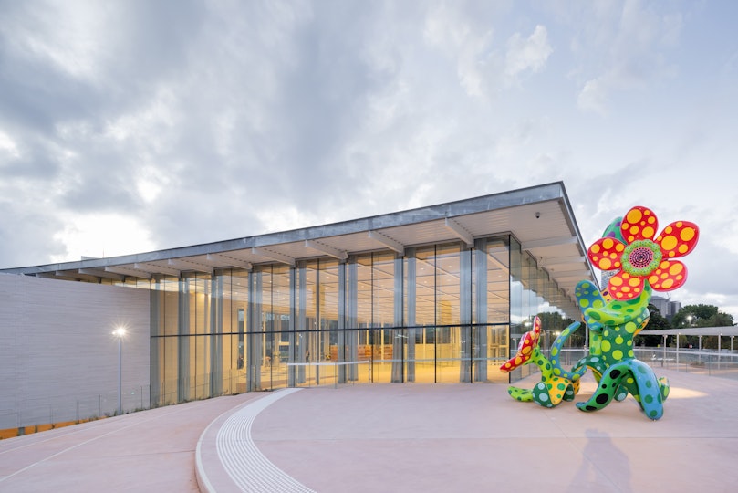 A large sculpture of spotted flowers on a terrace outside of a glass-walled building