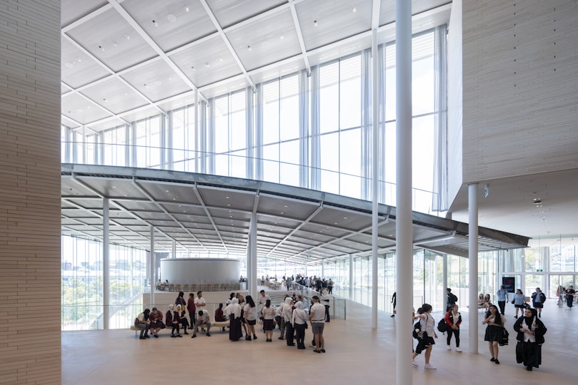 School students inside a large glass-walled building with an internal curved roof