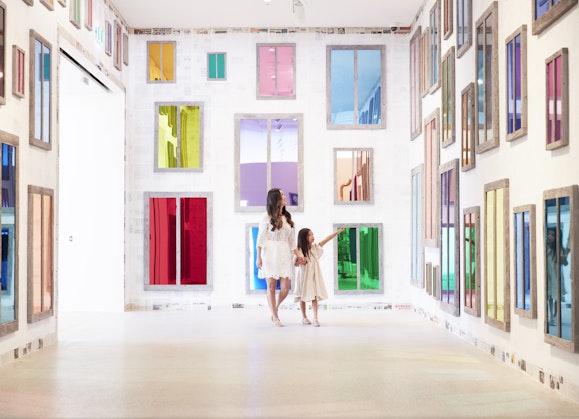 An adult and a child in a room full of coloured mirror-like windows