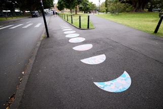 Decals shaped like the moon in different phases are stuck in a row on a footpath