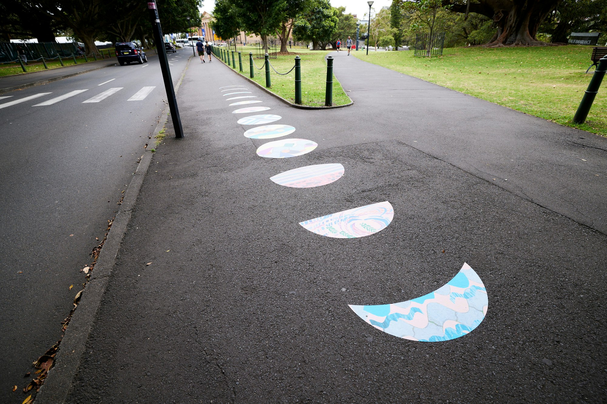 Decals shaped like the moon in different phases are stuck in a row on a footpath