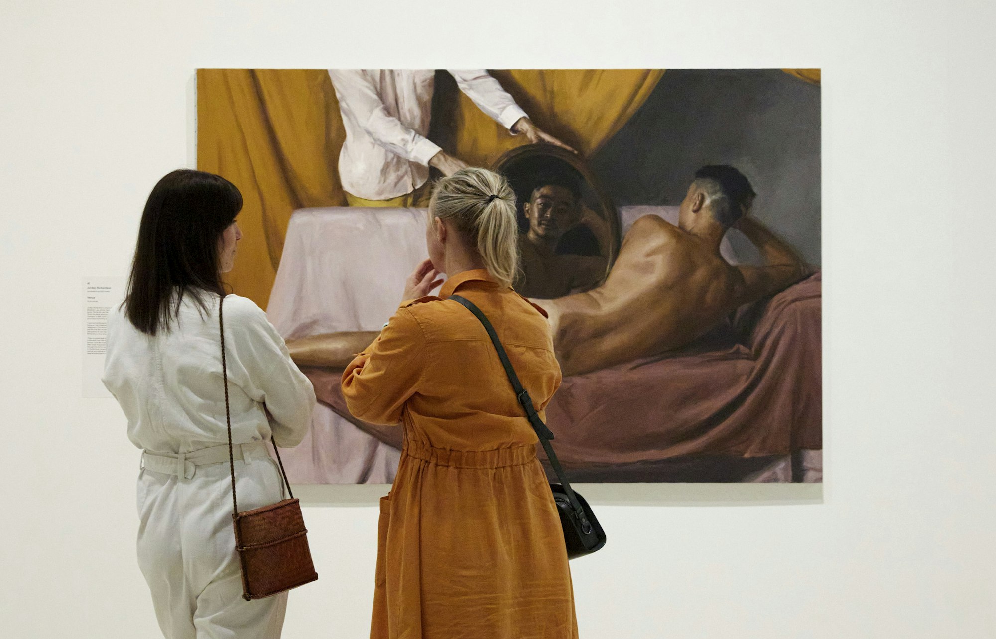 Two people look at a painting of a nude reclining on a sofa