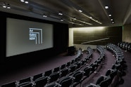 An auditorium with tiered seating and a large screen and podium