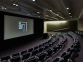 An auditorium with tiered seating and a large screen and podium