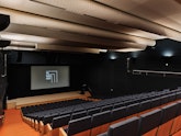 A large auditorium with tiered seating and a large screen and podium
