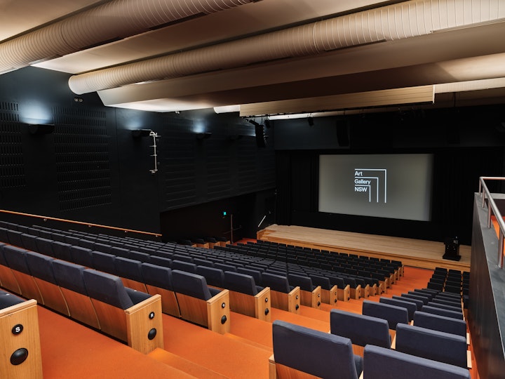 A large auditorium with tiered seating and a large screen and podium