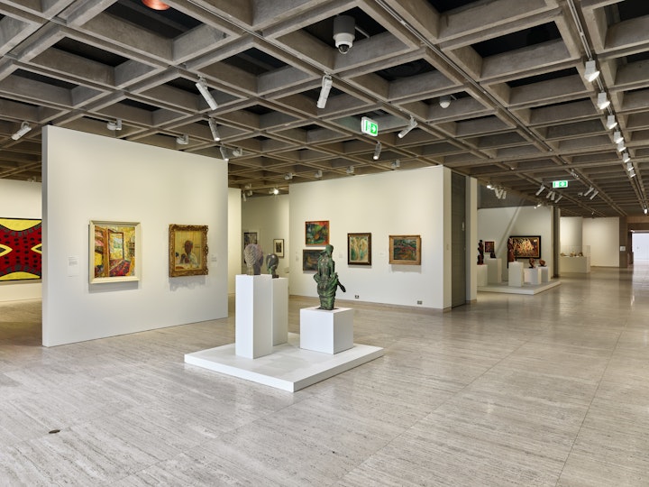 A gallery space with small sculptures on plinths and framed paintings on several internal walls