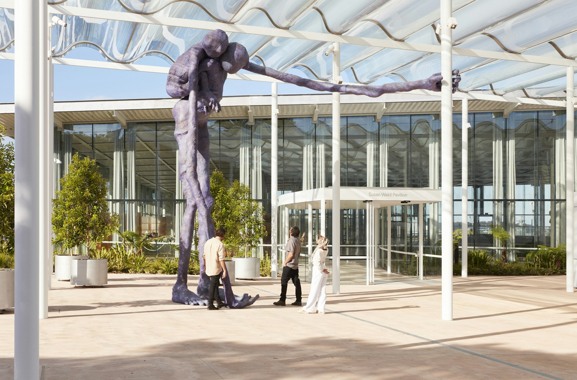 Three people with an enormous purple sculpture of a figure carrying another figure on its back