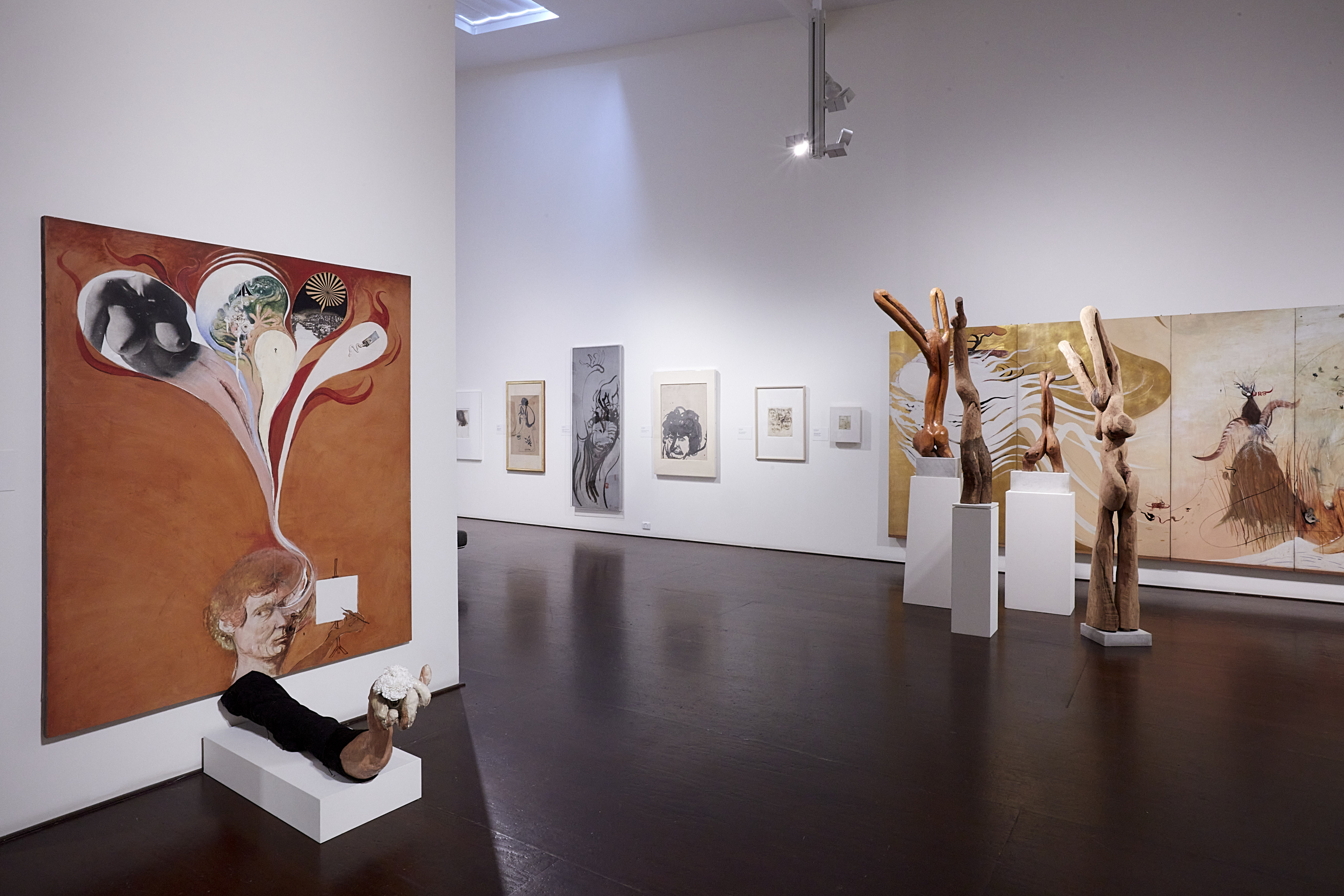 A large room containing paintings, drawings and  wooden sculptures by Brett Whiteley.