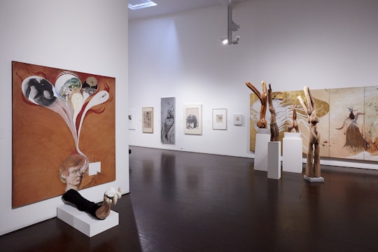 A large room containing paintings, drawings and  wooden sculptures by Brett Whiteley.