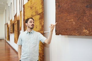 A person stands pointing at one of several large flat metal objects hanging on a wall
