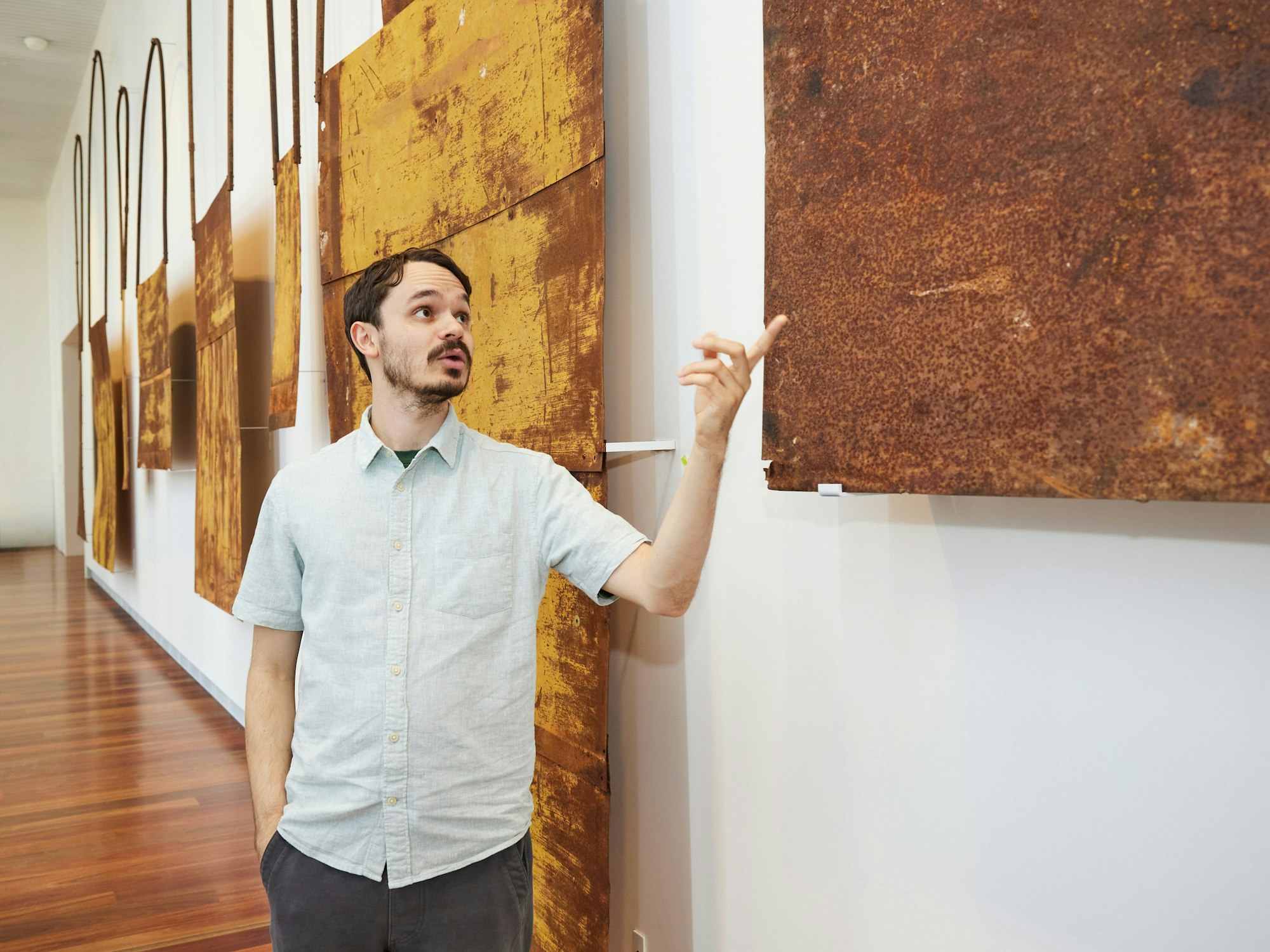 A person stands pointing at one of several large flat metal objects hanging on a wall