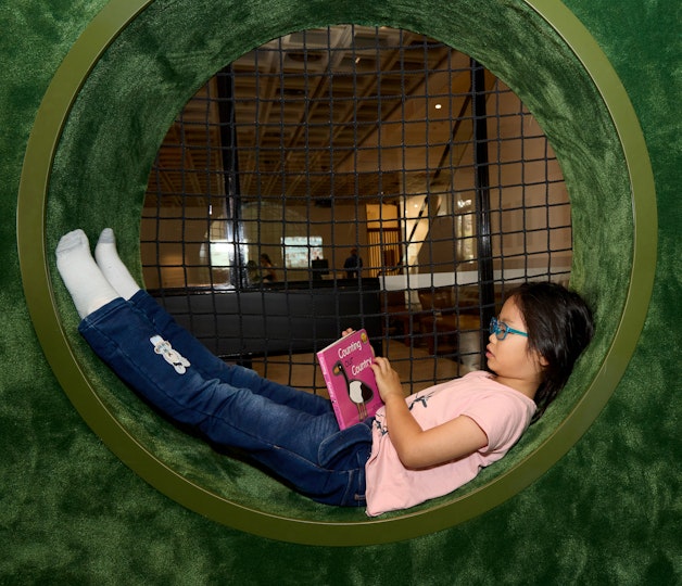 A child lies reading a book in a circular nook