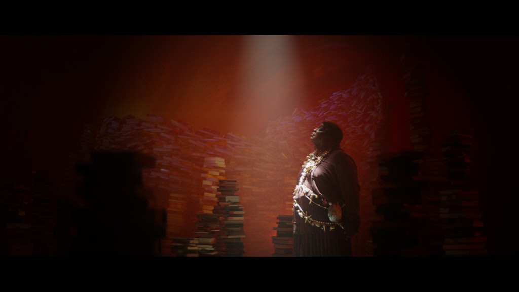 A person in a room with piles of books looks up towards a source of light